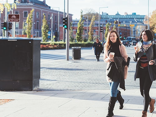 Two women with mugs of coffee walking in the center of Oslo