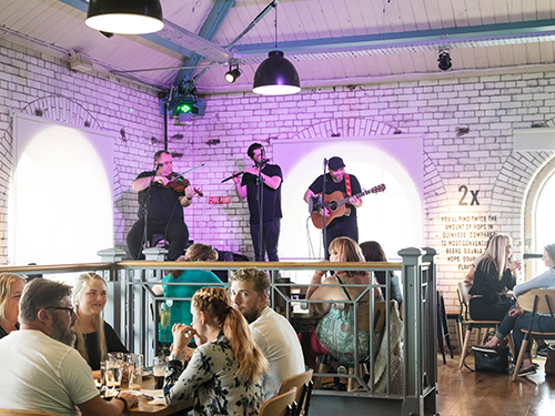 An interior scene of a venue in Dublin where people are eating and drinking, and musicians are playing 
