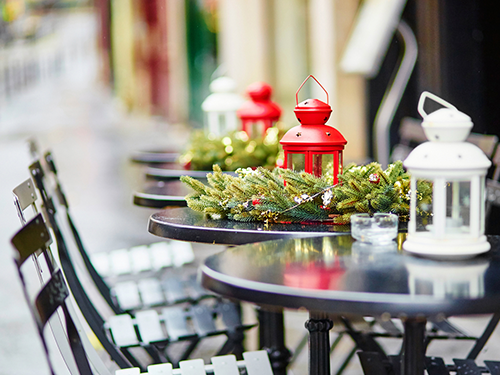 A couple of tables are positioned outside of a cafe in Paris, with red flowers on the table