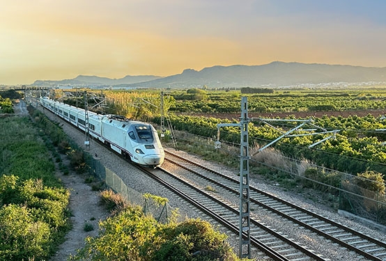 A train drives through beautiful scenery with a mountain backdrop close to Barcelona.