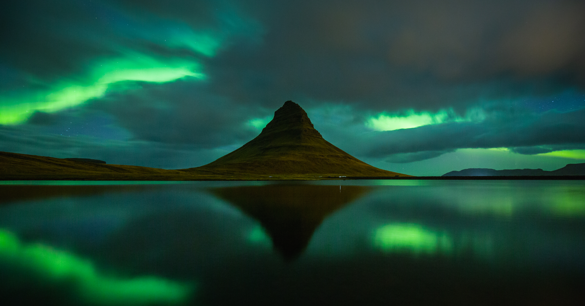 the aurora borealis dances in the sky and is reflected in the water at Kirkjufell mountain on snæfellsnes peninsula