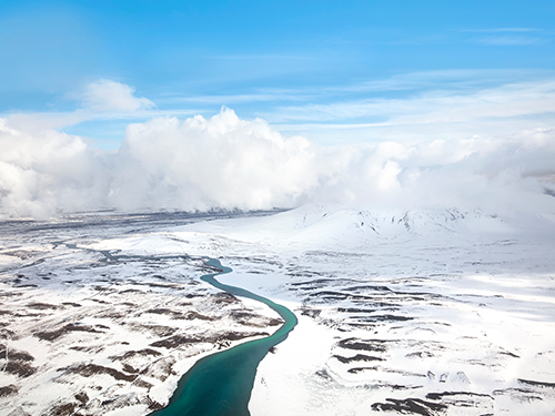 An overhead shot of a blue river running through a snowy landscape in the Westfjords of Iceland 