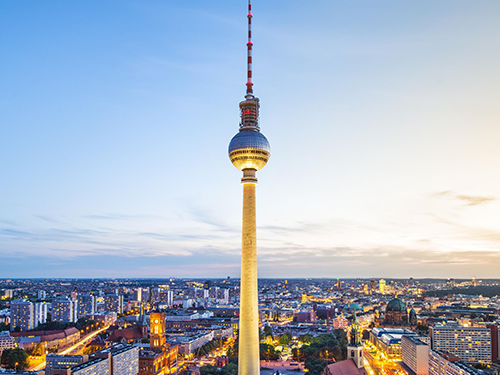A skyline of Berlin with city lights lit up against the dusky evening light with Berliner Fernsehturm: Berlin's Television Tower, in center shot