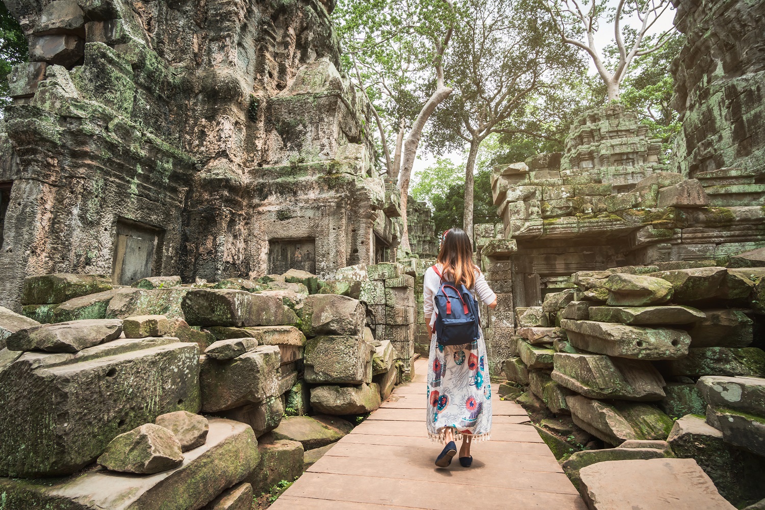 A person with a blue backback walks through a pathway at an ancient ruin site