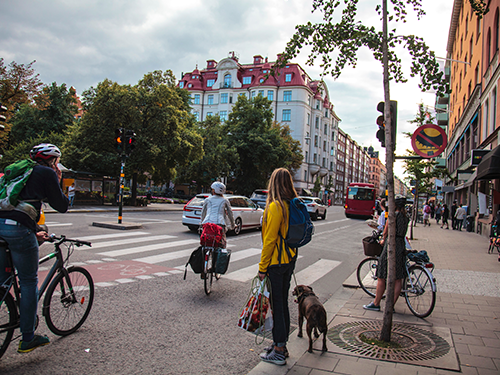 A street view of downtown Stockholm where there are cars on the road, pedestrians walking, and cyclists on bikes