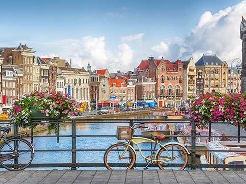 A bike is parked against a handrail in Amsterdam, with a view of one of the canals in the background