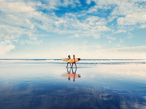 Two people walk on the beach in Tenerife holding surf boards
