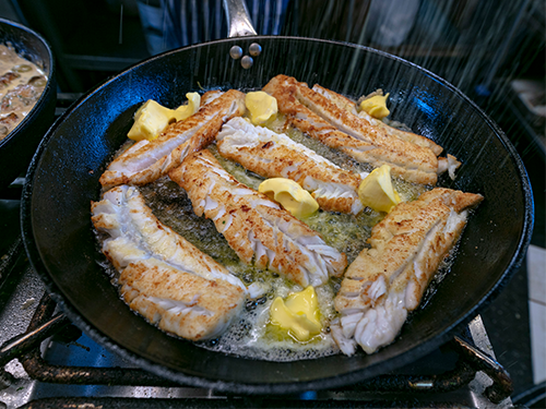 A black pan full of several pieces of white fish fried in butter, as pictured in Tjöruhúsið