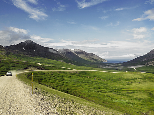 Een auto rijdt door de Eastfjords naar de camera toe, met fjorden op de achtergrond 