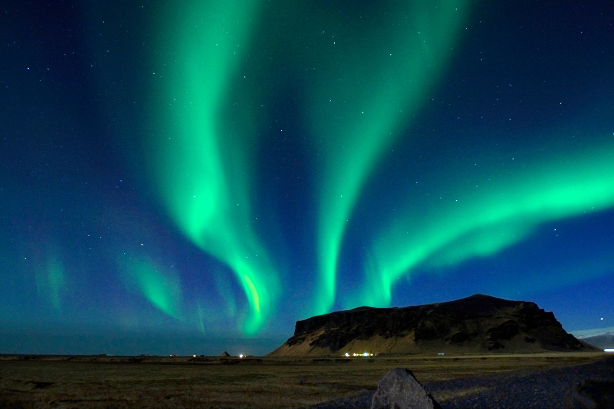 the aurora borealis appears in streaming waves above a mountain in South Iceland