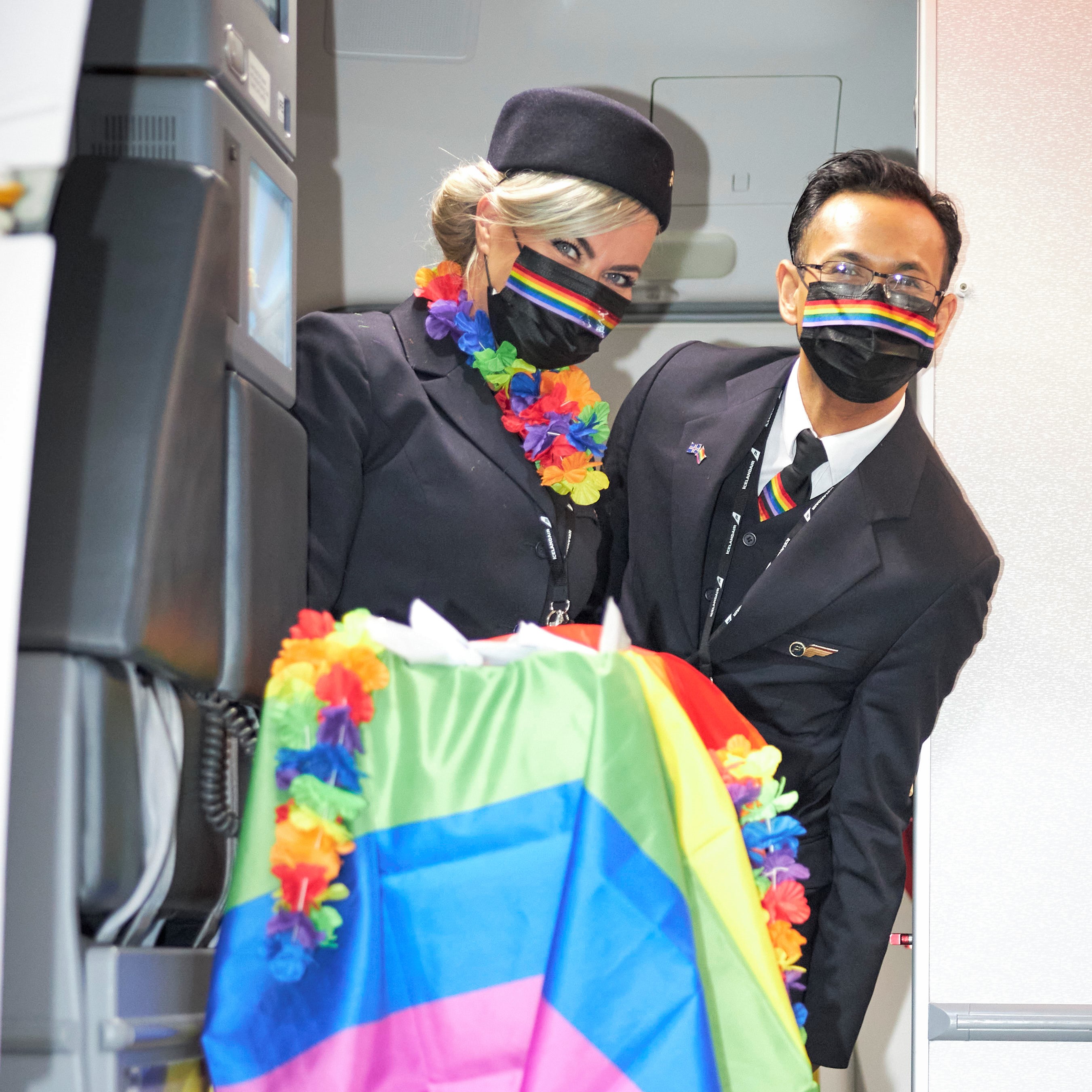 two members of Icelandair cabin crew standing in the aircraft next to the main entry door, with the cabin trolley covered in a rainbow flag