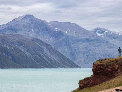 a statue of a viking settler stands dramatically on a mountain in Greenland, looking over the landscape