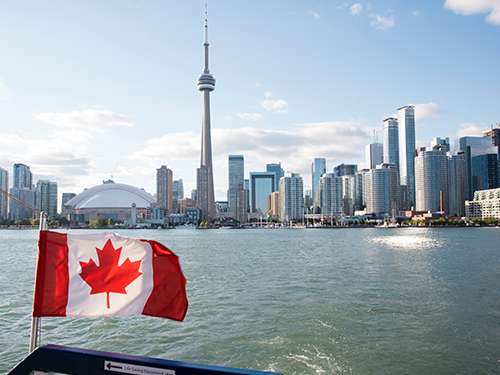 A view of Toronto’s city scape, as seen from a boat with a Canadian flag in the foreground 