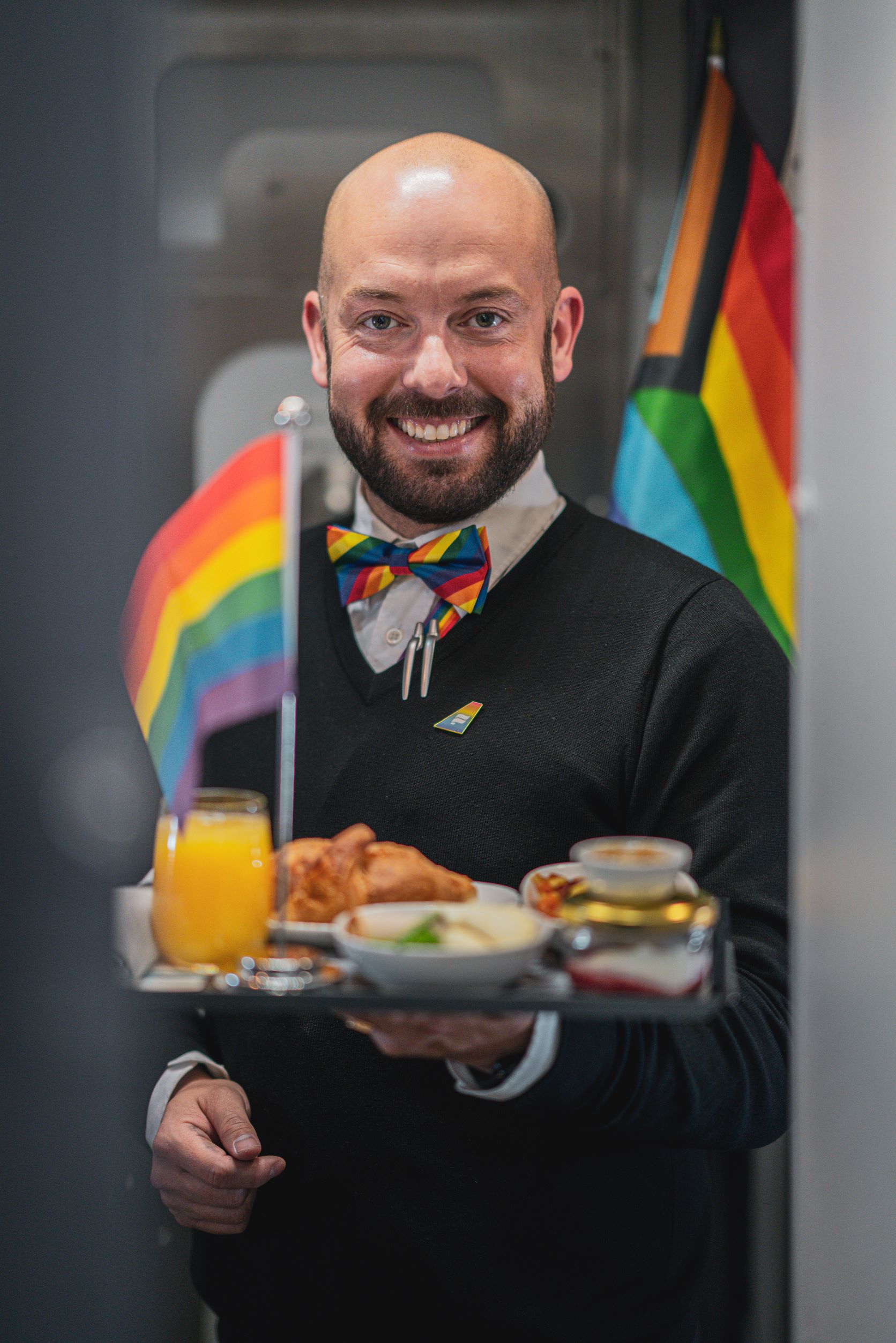 Icelandair Pride flight 2022: cabin crew member serves a tray of food, with rainbow flags in foreground and background