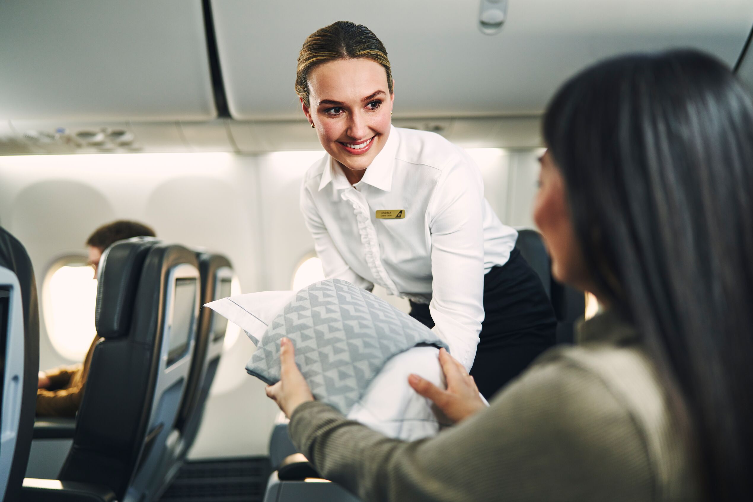 Photo of passengers in Saga Premium on board Icelandair aircraft. The passengers are receiving a blanket and pillow.