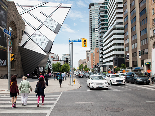 People walk across a zebra crossing in Toronto, with traffic appearing to have been stopped at the lights 