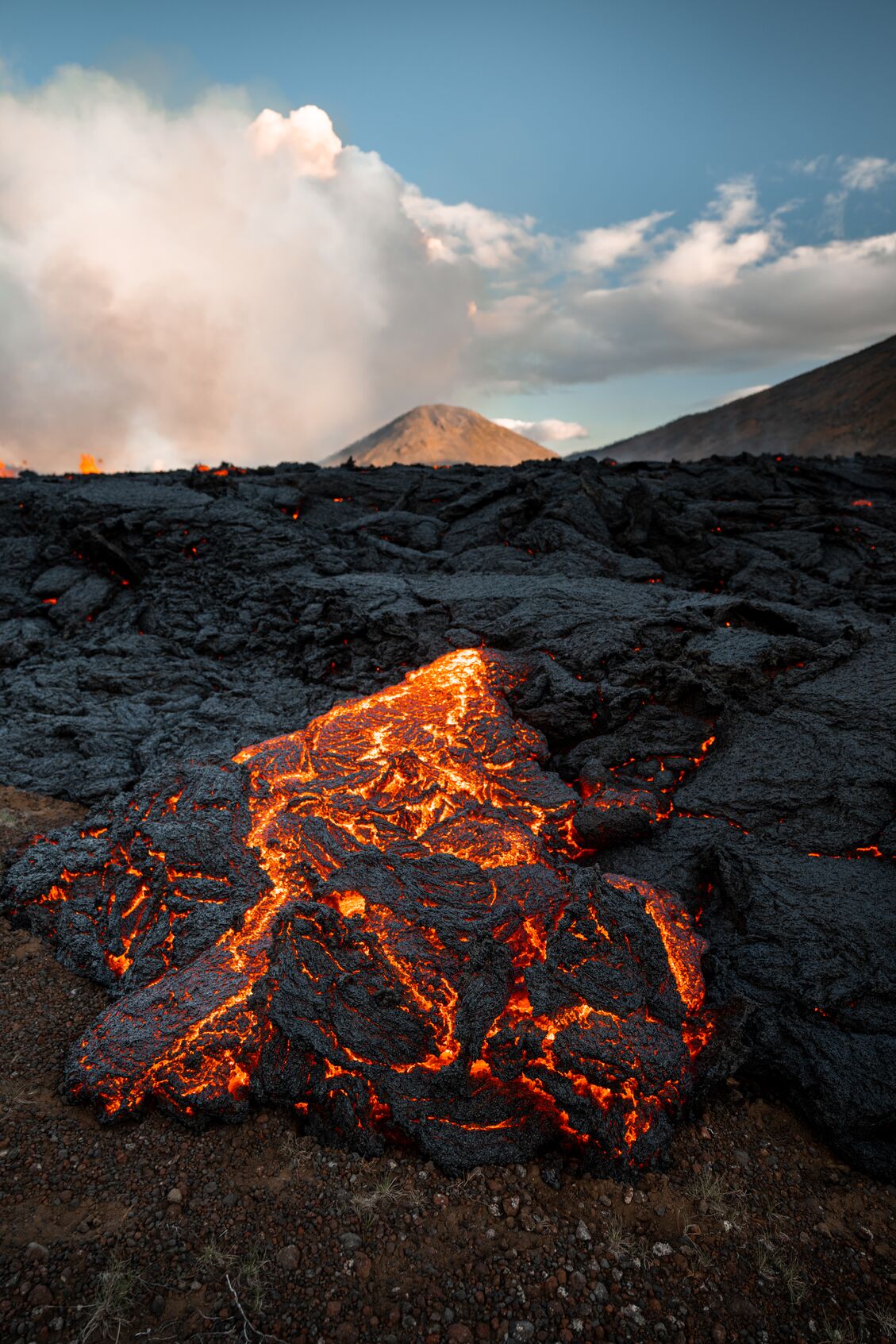 close-up image of red-hot lava field with erupting volcano in background