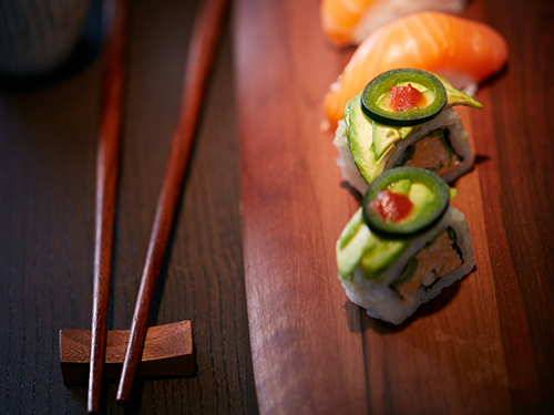 A wooden block with four pieces of sushi laid on it and two chopsticks laid out next to it 