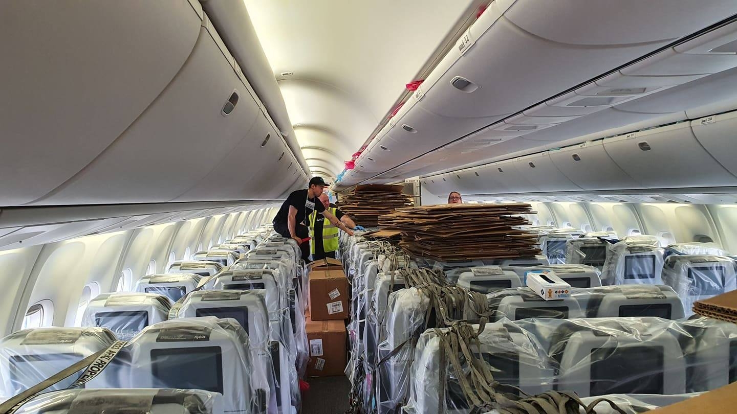 The aircraft interior shown with seats covered in plastic film and lots of boxes being filled with PPC supplies