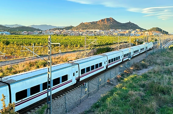 A train drives past a neighborhood located near beautiful hilltops.