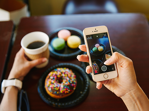 A picture of someone taking a picture on their smartphone of a doughnut and sweet treats laid out on the table in front