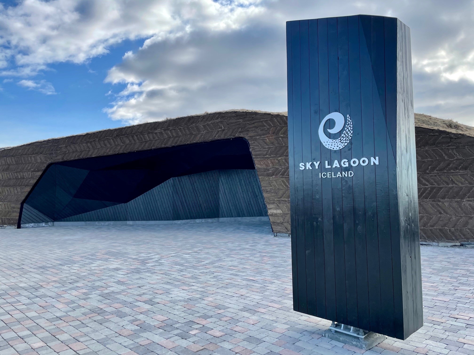 The exterior entrance of the Sky Lagoon in Reykjavik - a signpost stands before the rocky entrance