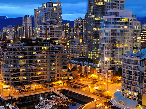 A harbour view of Vancouver, Canada, with lights from the high rise buildings lit up against the night sky 