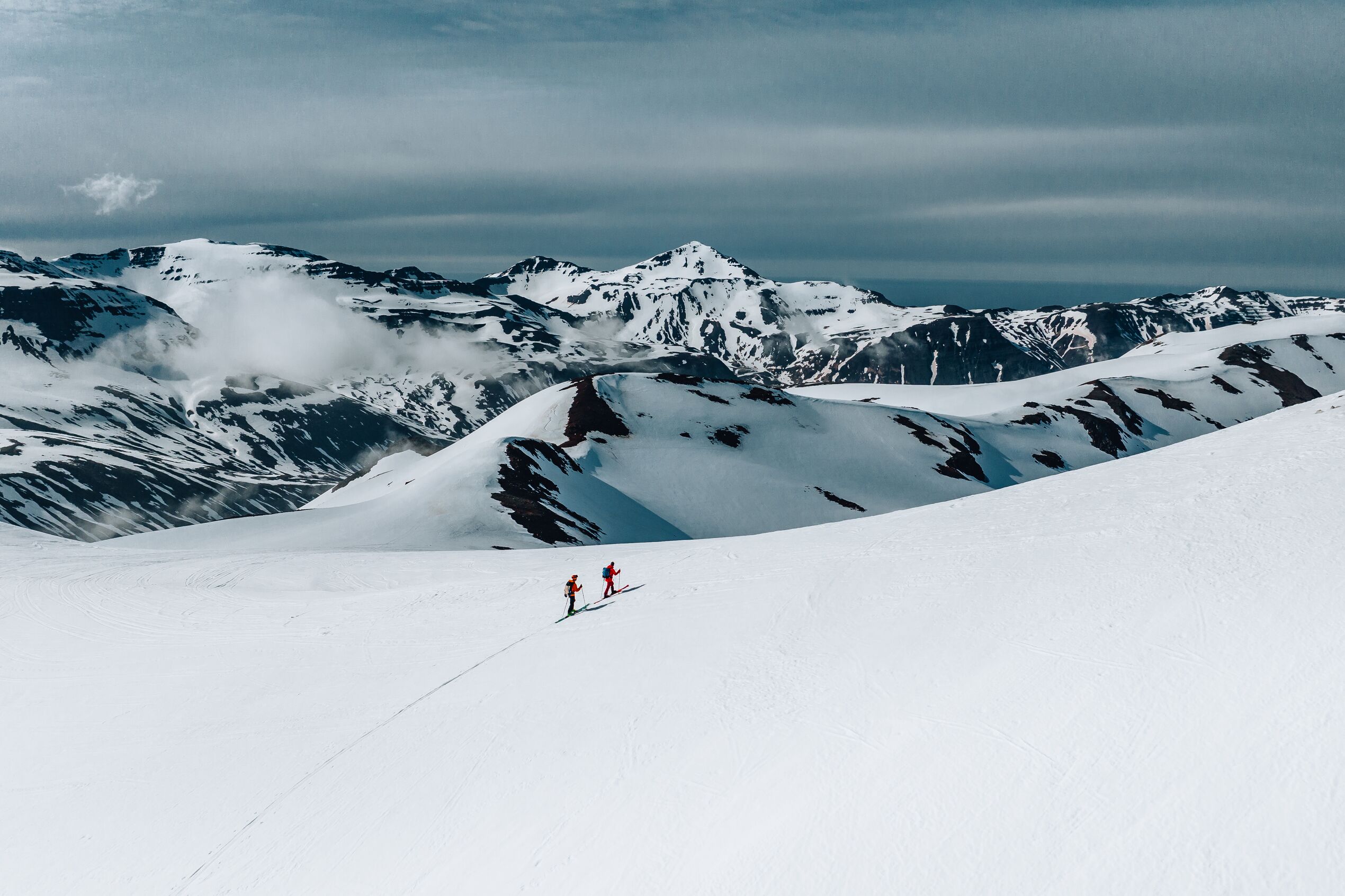 A distance shot of two skiers on a snowy mountain in North Iceland, with mountainscapes as a backdrop