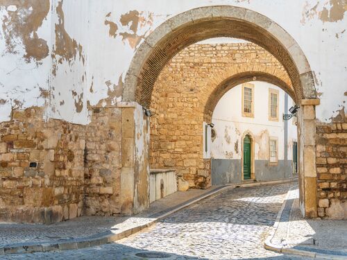 an old stone arch stretches over the cobbled streets of Faro