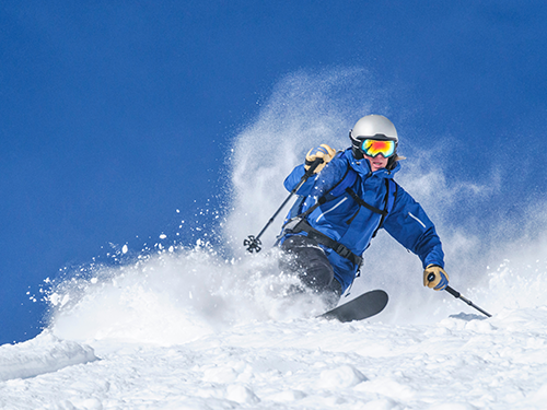A skier makes their way down the slopes, wearing a blue jacket and colourful visor.