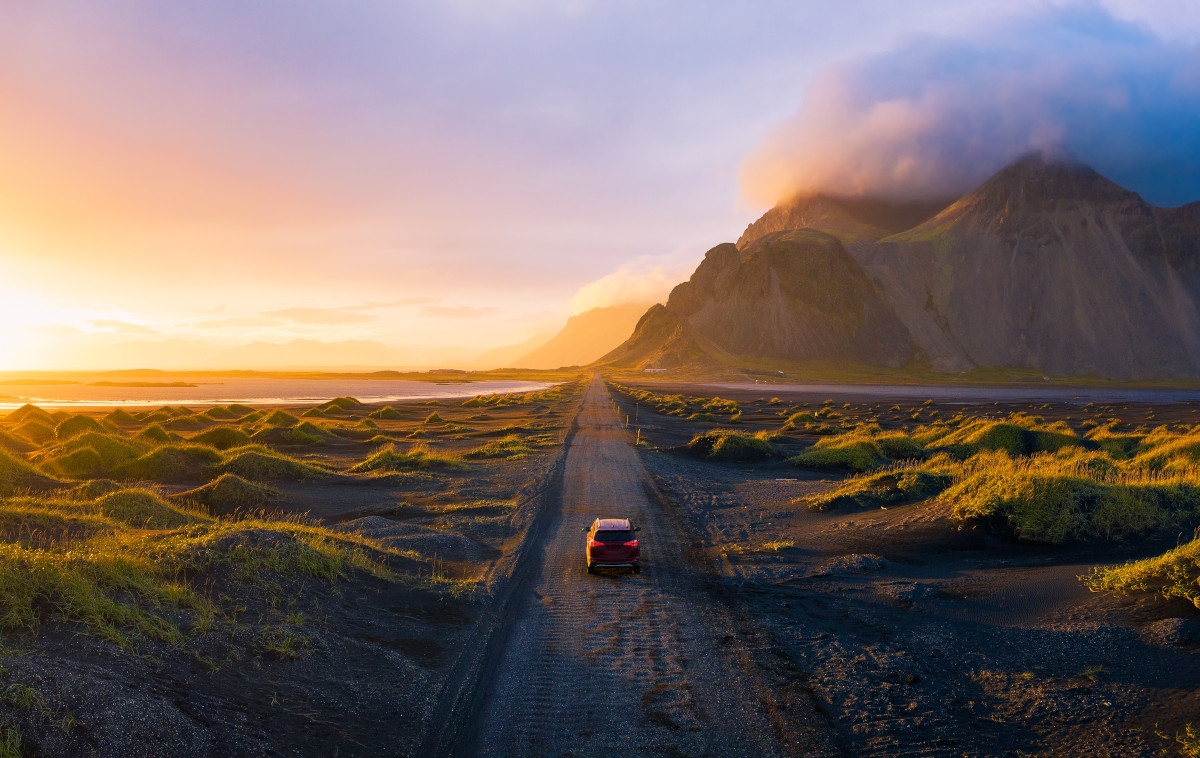 Bird's-eye view of a car on a mountain-lined road in Iceland with the sun sitting low on the horizon