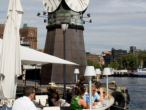 People drink and dine outside at a restaurant by the water in Oslo 