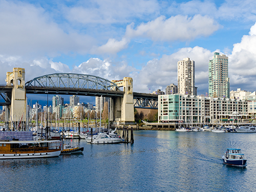A view of the Burrard Bridge in Vancouver, as pictured from across the water with boats and high rises in shot 