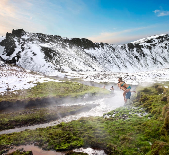 a couple, a woman piggybacking a man by Varmá river in Reykjadalur, warm river that runs through the snowy valley.