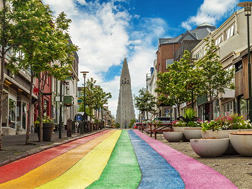 La rue arc-en-ciel à Reykjavík, Skólavörľustígur, photographiée ici avec l’église Hallgrímskirkja en arrière-plan et des magasins de chaque côté 