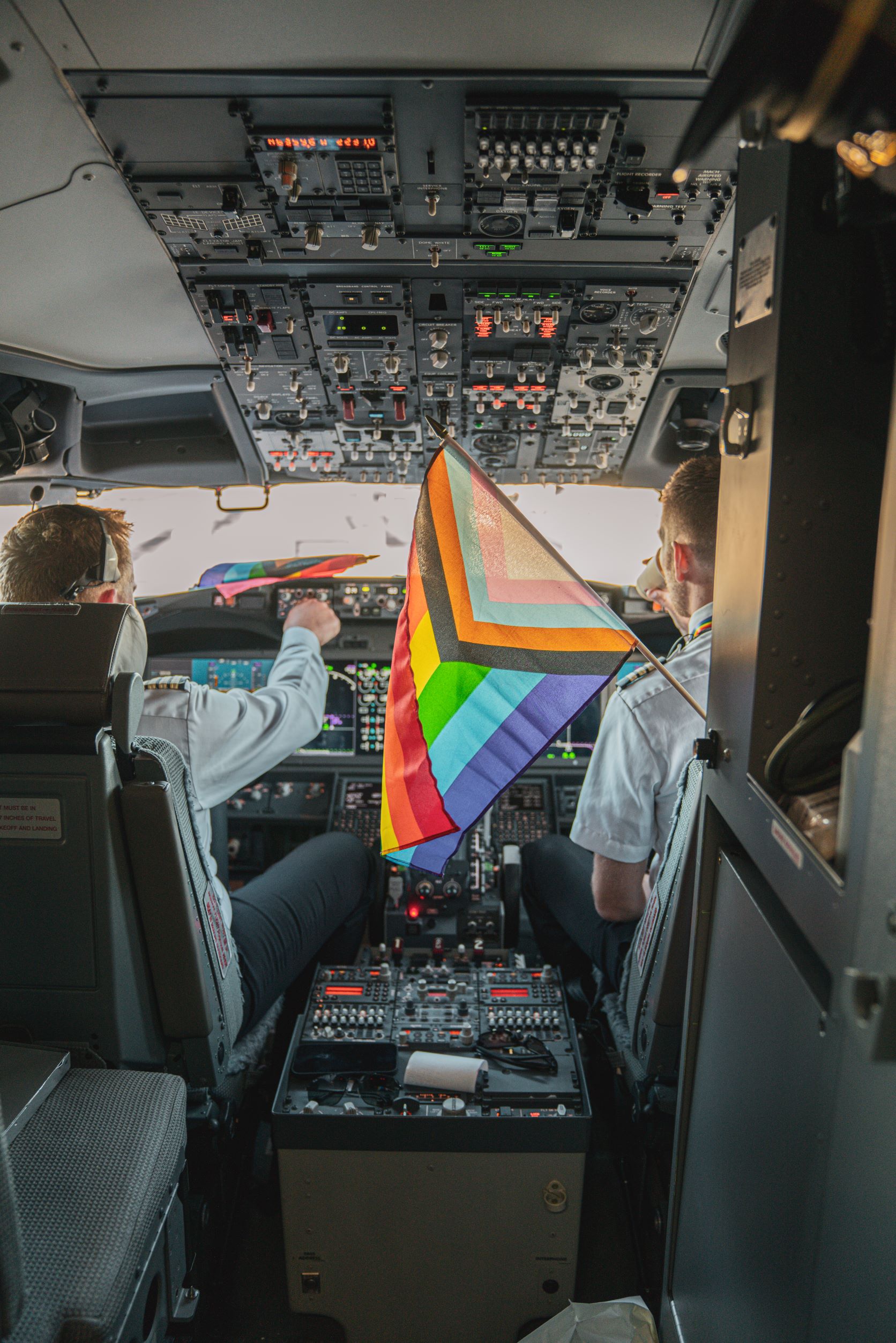 Icelandair Pride flight: cockpit view of 2 pilots, with rainbow flag flying in foreground