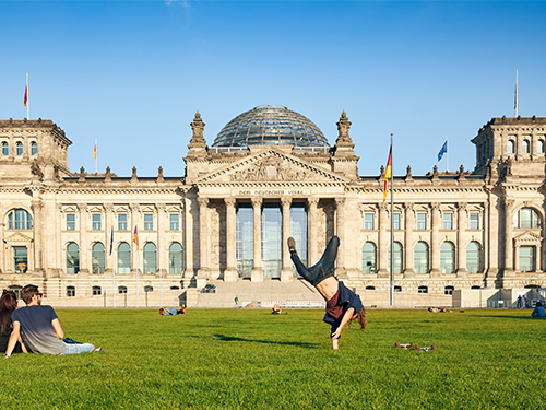 Ungur maður fer í handahlaup á grasflötinni fyrir framan Reichstag bygginguna í miðborg Berlínar