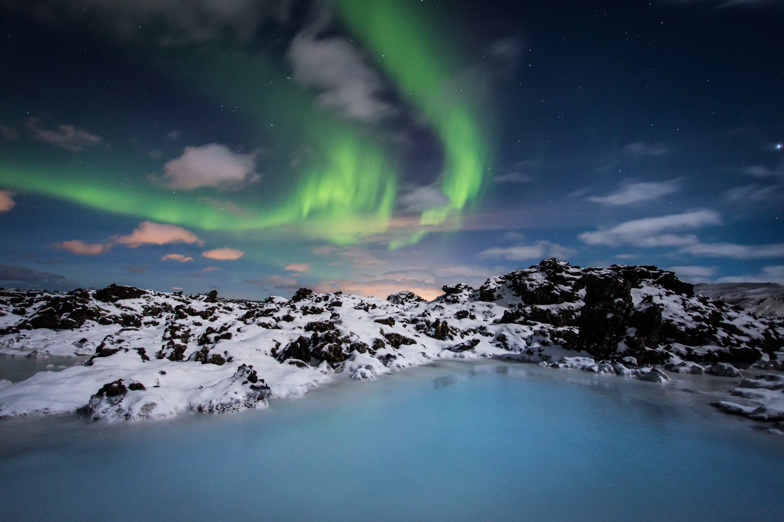 The milky blue water of the blue lagoon pictured with northern lights overhead