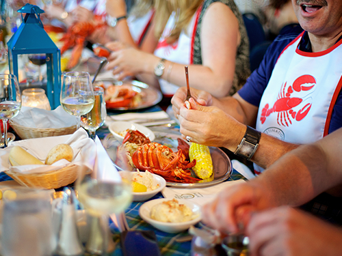 Een groep mensen met een servet met afgebeelde rode kreeft eet kreeft in Nova Scotia 