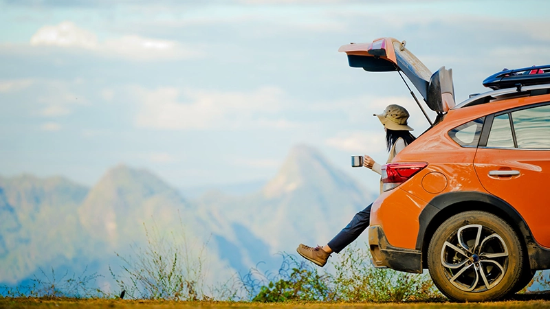 a woman enjoying a mountain view from her orange car