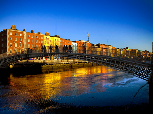 The Ha’Penny Bridge in Dublin, Ireland, pictured here with people walking across it as as dusk settles upon the city 