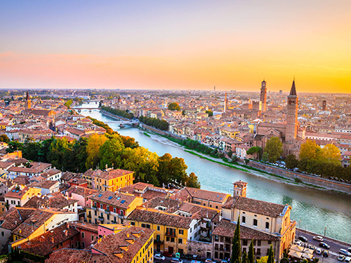A view of the city of Verona, pictured from above at sunset with a dusky pink sky
