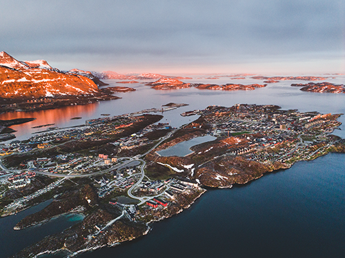 A birds eye view of the city of Nuuk lit up in dusky pink evening light 