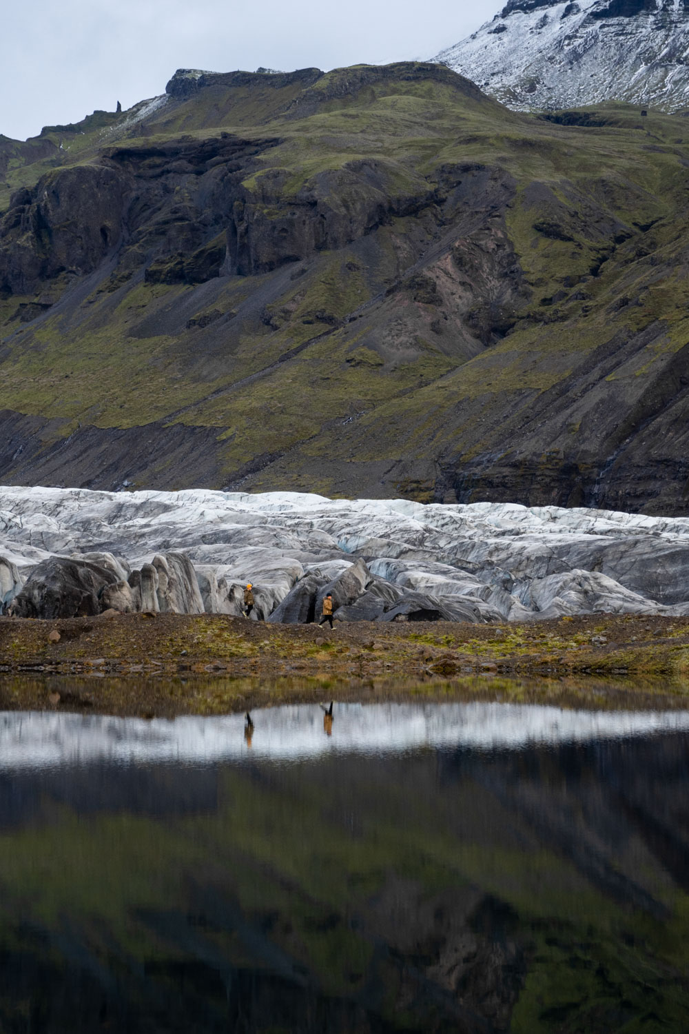 Chris Burkard's 2 sons play in front of a glacier backed by a mountain at Svínafellsjökull. The mountain is reflected in the lake of water in the foreground