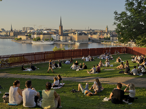 People lie in the grass at Ivar Los park in Stockholm, overlooking a view of the city skyline