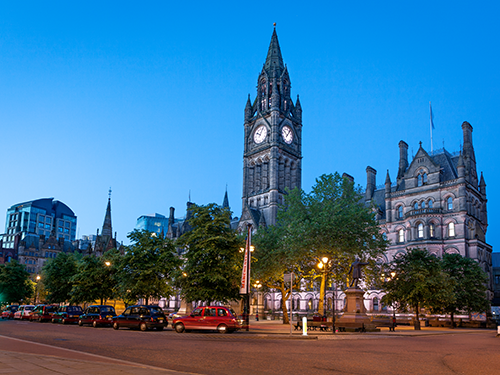 A streetview of downtown Manchester with taxis lined up at the end of an evening 