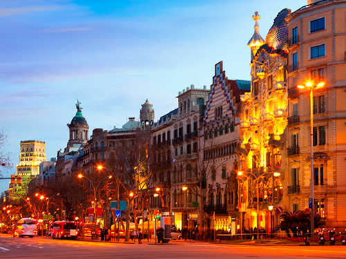 A busy city street in Barcelona, with cars and buses driving on the road, here pictured in the evening light 