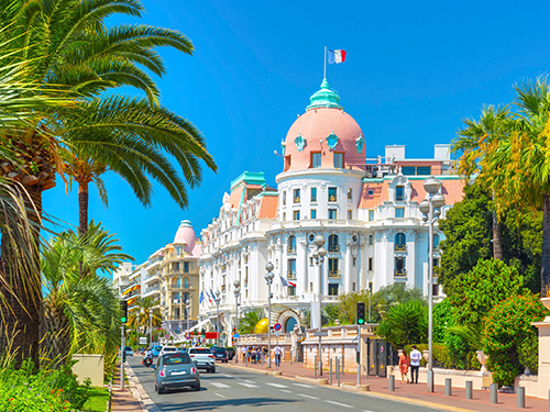Promenade de Anglais in Nice, France pictured here on a bright sunny day with cars driving by and people walking on the street 