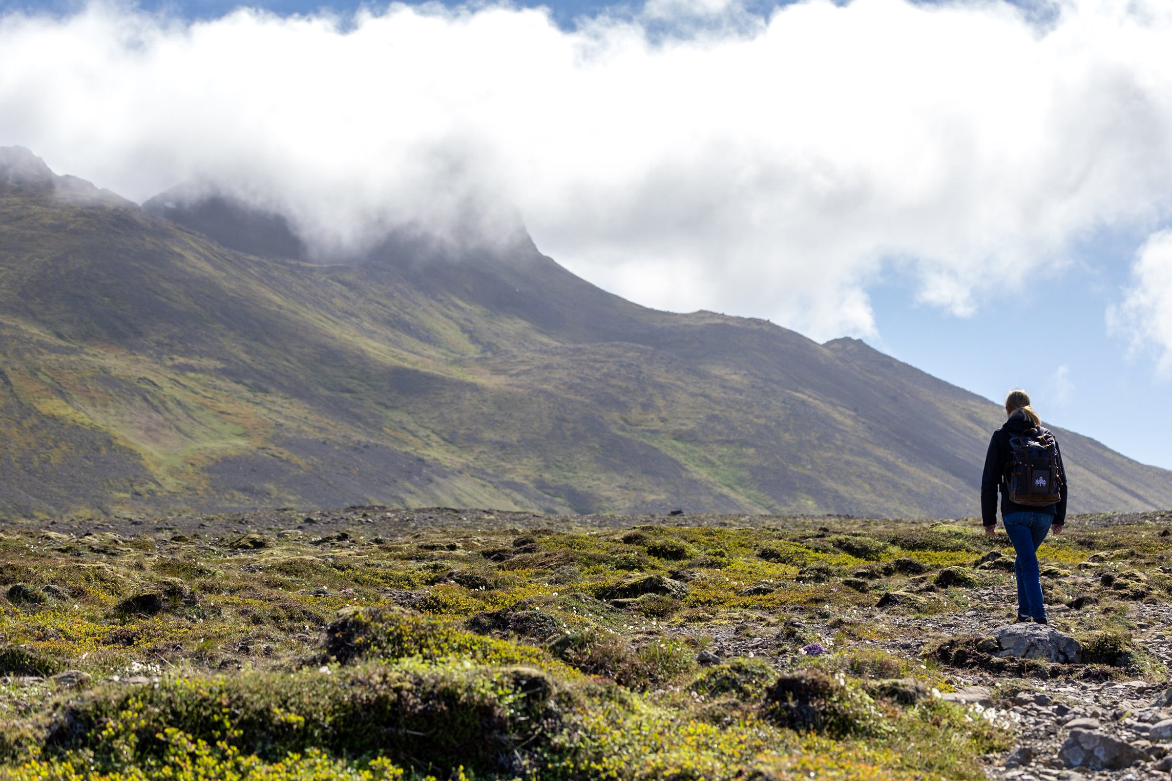 A woman hikes over mossy ground with a mountain in the background