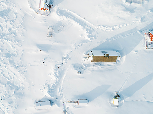 A birds eye view of a snowy landscape of Ilulissat, Greenland, with track marks in the snow and colourful houses underneath 